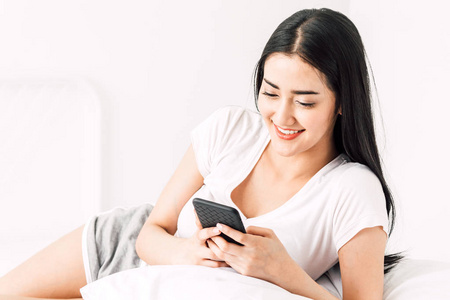 快乐的女人放松和使用智能手机在床上的家庭. 女人用智能手机检查社交应用程序