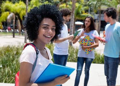 聪明的拉丁美洲女学生与小组学生户外在大学校园在夏天