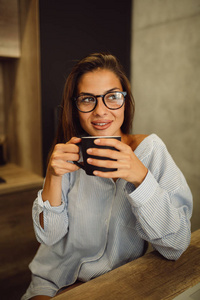 戴眼镜的漂亮女孩的肖像在厨房里喝着早晨的咖啡