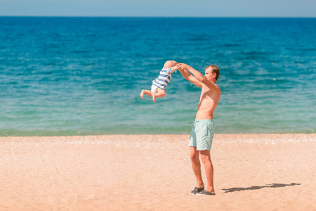 年轻快乐的父亲在沙滩上和他的孩子玩耍。婴儿转过身, 旋转着