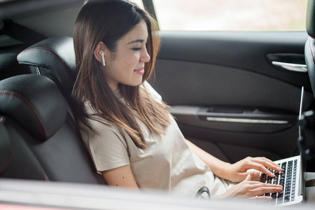美丽的年轻亚洲妇女在汽车使用笔记本电脑
