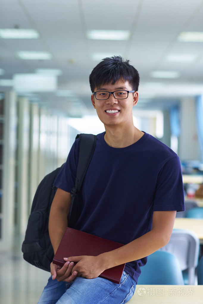 年轻的男大学生看图书馆中的相机微笑
