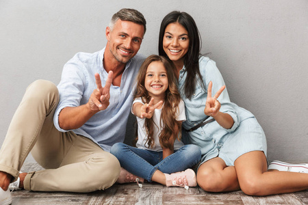 一个幸福的家庭的肖像父亲, 母亲, 小女儿拥抱, 而坐在一起, 显示和平姿态孤立的灰色背景