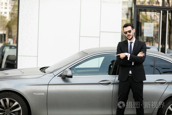 优雅的商人站在外面与折叠的武器 私人司机等待他的老板指向豪华轿车