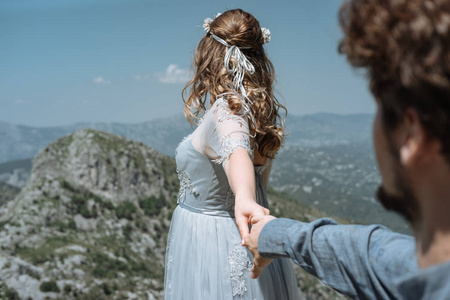 时尚浪漫情侣对山的背景。跟我来。新娘牵着新郎的手