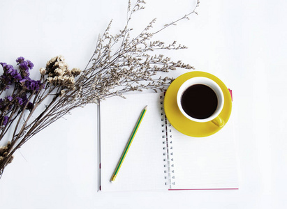 黄色陶瓷咖啡杯和铅笔放在打开的书, 旁边干花, 在白色表