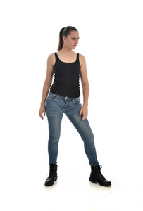 穿黑色单和牛仔裤的黑发女孩的全长肖像。站立姿势。在白色工作室背景下被隔离