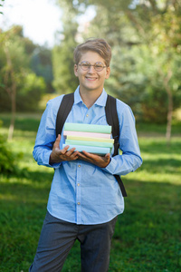 非常可爱, 小男孩在圆眼镜和蓝色衬衣与背包在公园里存放书。教育, 回到学校概念