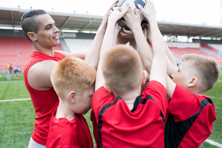 少年足球队的肖像在户外体育场赢得比赛后, 一起捧着球, 开心地欢呼。