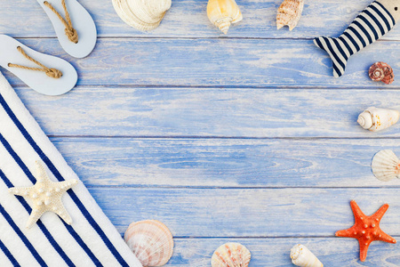 创意平躺的概念, 暑期旅游假期。毛巾翻转拖鞋上图贝壳和海星在柔和的蓝色木木板背景与拷贝空间在质朴样式框架模板文本