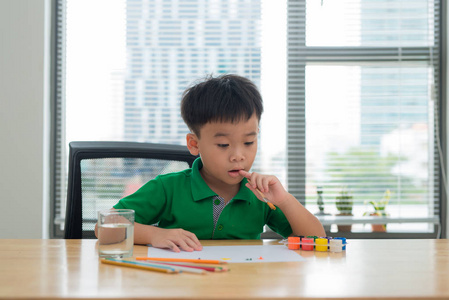 孩子们在学习桌上思考。孩子拿着一支钢笔和一本笔记本, 思考脸部动作。男孩做功课在学习桌与想法行动