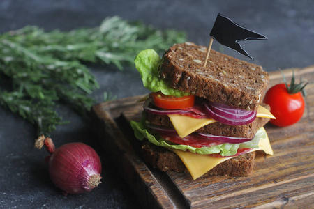 美味的三明治由面包, 西红柿, 香肠, 洋葱和生菜在木板和深色背景, 选择性聚焦