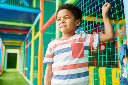 腰部的可爱的非洲裔美国男孩的肖像靠在网上和微笑的乐趣儿童游戏中心
