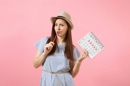 穿着蓝色连衣裙的年轻女子的肖像, 戴着红色铅笔的帽子, 女性月经日历, 用于检查在粉红色背景下的月经天数。医疗保健妇科概念。复制