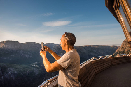 一个极端计划的肖像旅行为英俊的老人在 kjerag 的石头上的 kjeragbolten 挪威, 自拍在你的自由手中手持智能手机