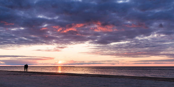 海滩上的男人和女人。夕阳下的人的剪影。波罗的海