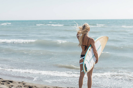 美丽的年轻白种女孩站在沙滩上与冲浪板的背面视图