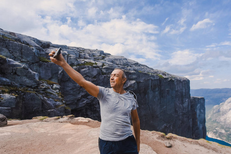 一个极端计划的肖像旅行为英俊的老人在 kjerag 的石头上的 kjeragbolten 挪威, 自拍在你的自由手中手持智能手机