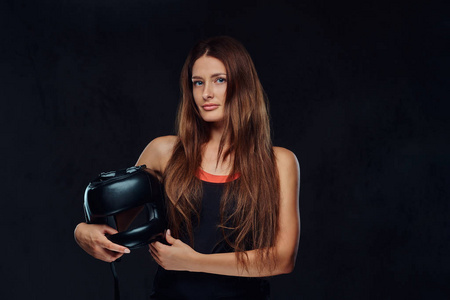 一个漂亮的黑发女拳击手的肖像在运动装着一个防护头盔, 看着相机。在深色纹理背景下隔离
