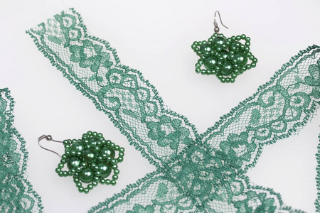手工制作的珠子耳环。在家里做针线活。珠首饰。绿色。在白色背景和花边丝带