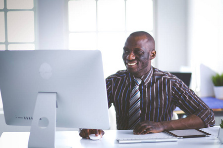 在经典西装的英俊非裔美国商人是使用一台笔记本电脑和微笑在办公室工作的时候