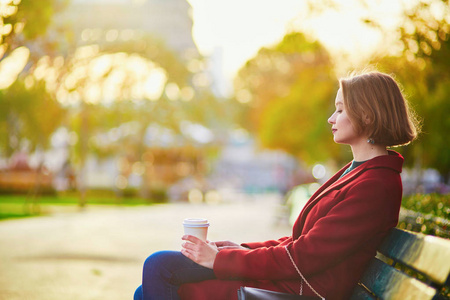 一个美丽的年轻法国妇女坐在长椅上, 喝咖啡附近的埃菲尔铁塔在巴黎的秋季一天