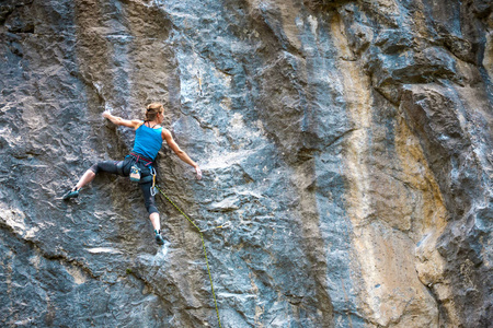 登山者正在训练攀登岩石。坚强的女孩克服了艰难的攀登路线。积极的生活方式。极端的爱好。女人在大自然中参加体育运动