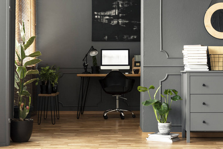 在办公桌上的黑色绘画与台灯和台式电脑在灰色公寓内部。真实照片