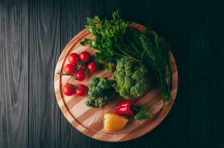 新鲜蔬菜 樱桃西红柿, 花椰菜, 胡椒, 莳萝, 欧芹, 在一个圆形木板上, 在一个黑色的木桌上。食谱。成分。膳食食品。放置在