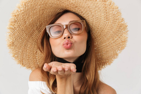 可爱诱人的女人的肖像20s 戴着大草帽和太阳镜吹空气吻在相机隔绝白色背景
