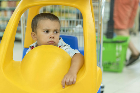 可爱可悲的小2岁男婴在超市的小玩具车, 爸爸或家长推孩子购物车车与他的儿子, 孩子第一经验的概念