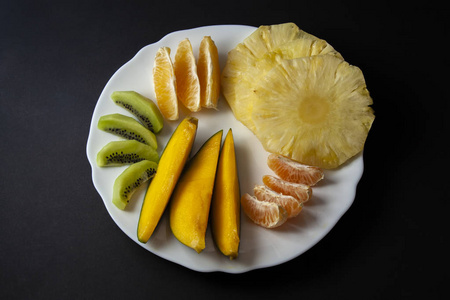 热带水果, 猕猴桃, 芒果, 菠萝, 橙色和柑橘片放置在白色的板上孤立的黑色背景。顶部视图, 平躺