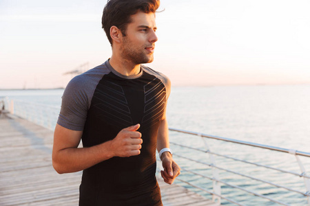 肌肉英俊男子20s 在运动服慢跑沿码头或海滨木板路在日出时的形象