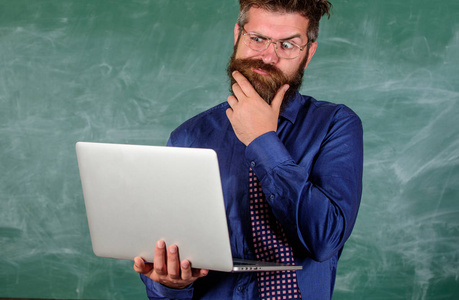 远程教育理念。时髦的老师戴眼镜和领带, 手提电脑上网。老师大胡子男子与现代笔记本电脑冲浪黑板背景。网上冲浪