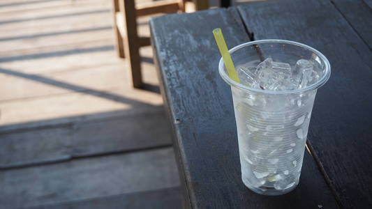塑料玻璃上有冰的纯净水的图像躺在老木桌上。用塑料制成的玻璃杯中的冰