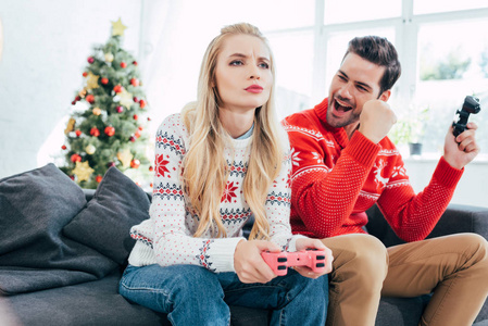 年轻夫妇玩游戏与操纵杆在家里与圣诞树