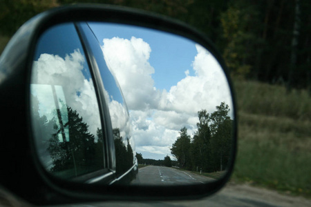 路上, 阳光明媚的夏日天空中有云彩和树木反射在汽车侧面镜子作为旅行背景