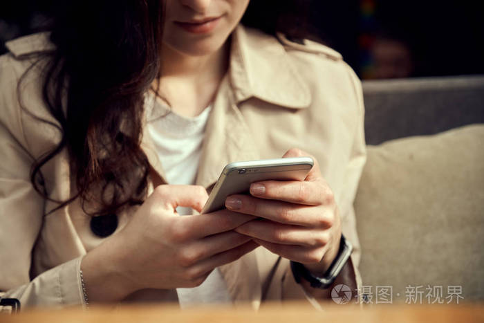 在咖啡歇的时候 一个漂亮的年轻女人在手机上看视频 一杯咖啡站在她