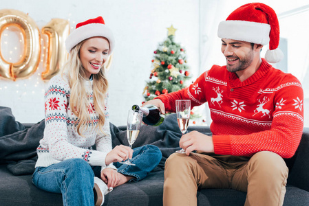 快乐的人在家里用圣诞树往杯子里倒香槟