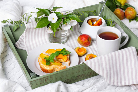 美味的土司面包与自制的杏果酱和杯茶在托盘上, 空心菜的花朵背景