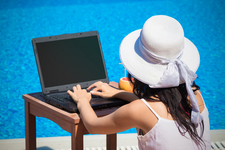 女性在游泳池旁边的空白屏幕笔记本电脑上工作