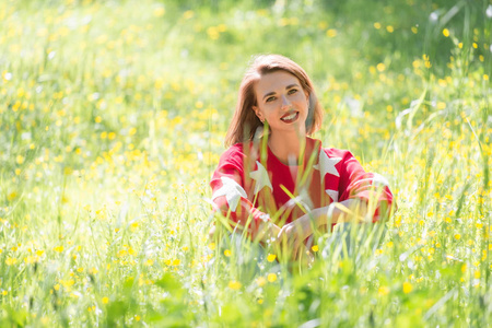 年轻英俊的女孩坐在草地上, 在阳光明媚的日子。公园红色毛衣的开朗放松妇女户外肖像