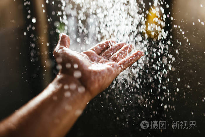 在阳光的照射下, 在黑暗的背景下, 一只手在水中喷洒.