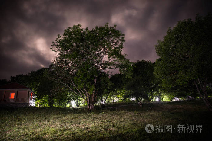 晚上在森林里建筑的山夜风景与月亮或老式乡下房子在晚上与云彩和星.
