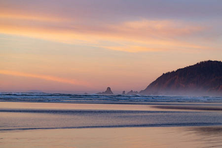 夕阳下的太平洋海滩与地平线上的山脉和岩石
