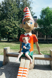 一个3岁的女孩在一个温暖的晴天坐在一个城市公园皮诺奇的木雕像上的肖像