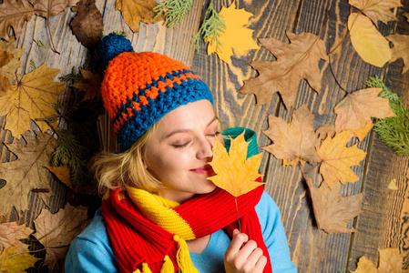愉快的时刻。秋天和秋天季节概念。时髦女子针织帽子和围巾举行秋叶。秋天舒适的气氛。女孩开朗的脸躺在木质背景与橙色叶顶部视图