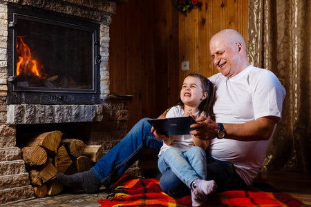 祖父和孙女使用数字平板电脑的乐趣坐在壁炉