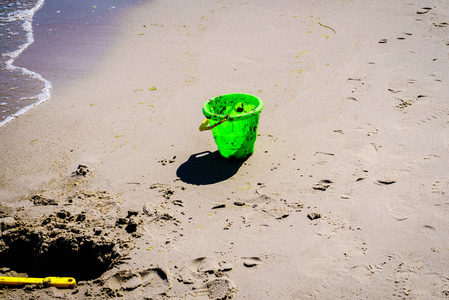 一个孩子在沙滩上留下的绿色玩具桶。有人在海边玩沙子