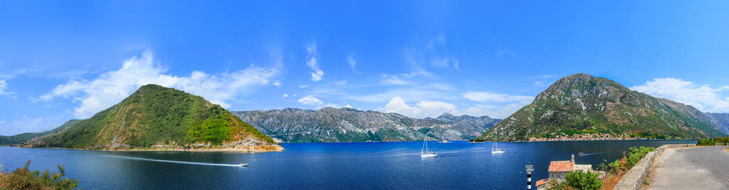 在海湾明亮的蓝色海湾周围的黑色山脉全景, 切割白色游艇。在这座小房子的脚下, 巨大的山脉在海湾和游艇的明亮的蓝色表面被反射。